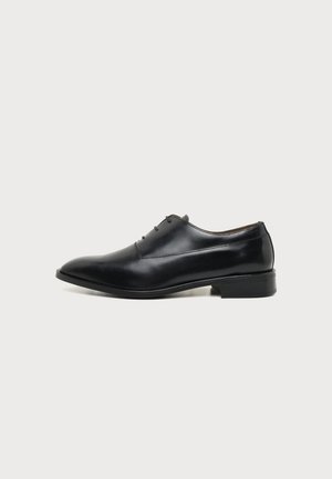 Chaussure habillée en cuir noir pour homme avec lacets, talon bas et surface lisse et polie, vue de profil sur un fond uni.
