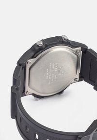 Relógio digital de plástico preto com fundo em aço inoxidável, apresentando dois botões prateados e uma pulseira texturizada com orifícios de ventilação.