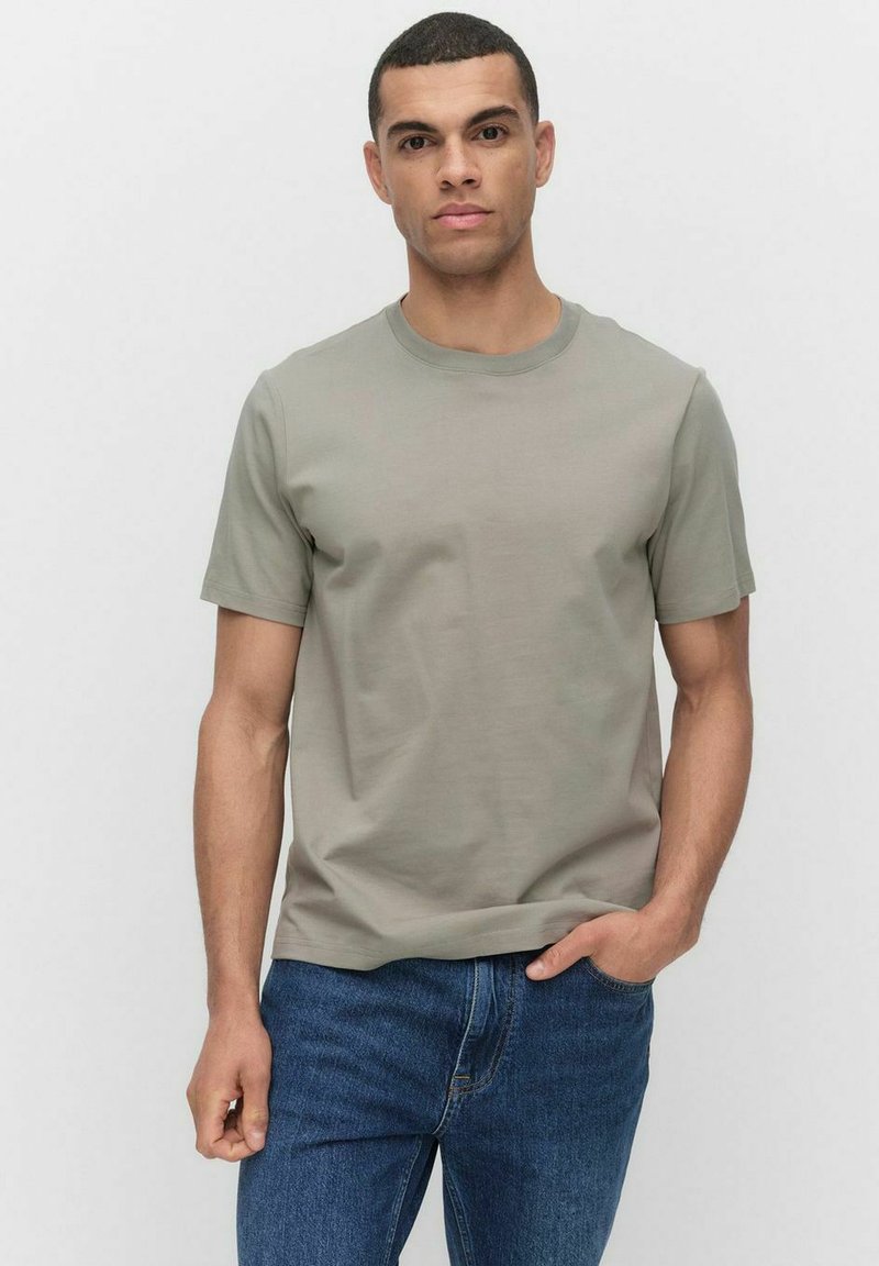Korte mouwen, ronde hals t-shirt in licht olijfgroen, gemaakt van zachte katoen, gecombineerd met donkerblauwe denim jeans. Klassieke, casual pasvorm.