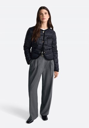 Doudoune noire avec un design matelassé, un col rond et des boutons dorés. Associée à un pantalon gris taille haute et des chaussures noires.
