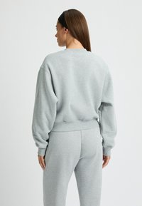 Sudadera gris claro con cuello redondo, puños y dobladillo acanalados, con un corte relajado. Combinada con pantalones de chándal a juego, de textura suave.