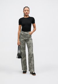 Top negro de manga corta con textura de canalé combinado con pantalones de pierna ancha de tiro alto con un patrón de rayas de cebra en blanco y negro. Zapatillas negras y bolso.
