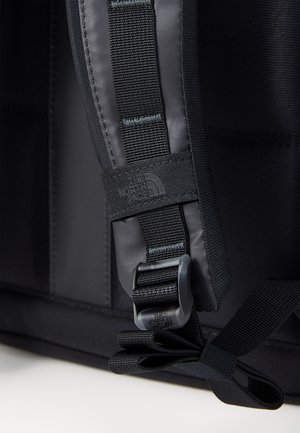 Gros plan d'une sangle de sac à dos noire avec une boucle réglable et un logo "The North Face" cousu sur la boucle en tissu.