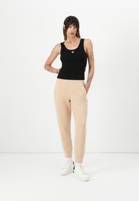 Svart åtsittande linne med rundad halsringning och en liten logotyp ovanför midjan, kombinerat med smala beigea sweatpants och vita sneakers.