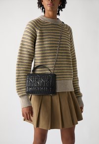 Schwarze gesteppte Handtasche mit einem oberen Griff und einer Kettenriemen, versehen mit einem dreieckigen Logo. Kombiniert mit einem gestreiften Pullover und einem plissierten Rock.