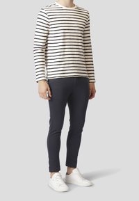 Camisa de manga larga a rayas en crema y marino, combinada con pantalones ajustados marinos y zapatillas blancas. Material de algodón, diseño casual, corte ajustado.