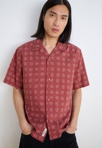 Camicia a maniche corte in tessuto borgogna con motivo a cuori bianchi e pois, dotata di bottoni frontalmente e una vestibilità rilassata. Etichetta sull'orlo.