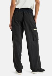 Black cargo pants with an elastic waistband, side pockets, and a reflective accent. Made from lightweight, smooth fabric; loose fit.