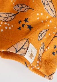 Baumwollstoff in warmem Orange mit schwarzen Blättern und Sternmustern, akzentuiert durch weiße Punkte; ausgestattet mit einem Etikett im Design eines Farbspritzers.