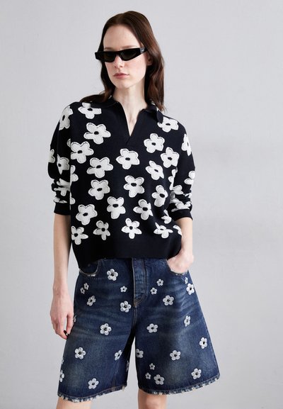 Must mustriga mustre valgete lillede borduuriga, paaritatud siniste denim lühikeste püksidega, millel on sarnased lillemustrid; mõlemad on mugava lõikega.