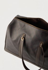 Tmavě hnědá kožená kabelka se zlatým zipem částečně otevřeným, dvěma uchy připevněnými zlatými kroužky, nakloněná proti světlému pozadí.