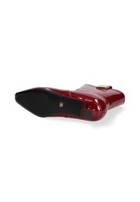 Stivale rosso con tacco alto, fromato lucido, punta affusolata e suola nera. Presenta un accento dorato sul lato e un tacco testurizzato.