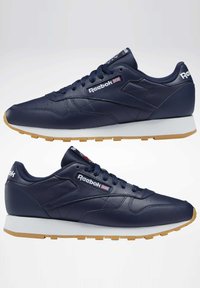 Tamsiai mėlyni odiniai sportbačiai su balta ir gumine išorine dalimi, su "Reebok" logotipu, raištelių dizainu ir lygiu paviršiumi.