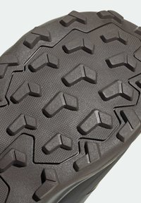 Gros plan de la semelle en caoutchouc noir avec des crampons en forme de V et un motif texturé pour chaussures d'extérieur ou de randonnée.