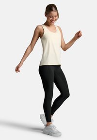 Top senza maniche di un beige chiaro abbinato a leggings neri. Il top presenta un girocollo; i leggings hanno dettagli delle cuciture e una vestibilità aderente.