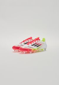 Soccer cleats with a white mesh upper, bright pink and neon yellow accents, black stripes, and translucent studs on a textured sole.