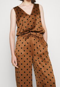 Tenue en satin marron à pois noirs. Comprend un haut sans manches à col en V, une taille élastique et un pantalon à cordon de serrage avec poches latérales.