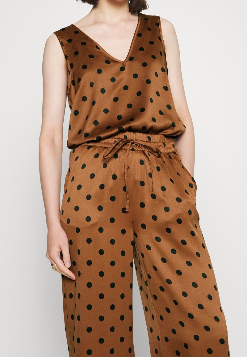 Tenue en satin marron à pois noirs. Comprend un haut sans manches à col en V, une taille élastique et un pantalon à cordon de serrage avec poches latérales.