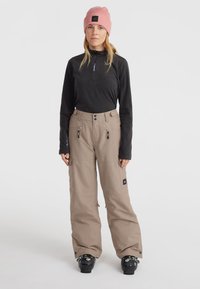 Ski outfit featuring a black long-sleeve zip top and beige snow pants with pockets, black footwear, and a pink beanie with a patch.