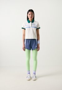 Camisola pólo branca com colarinho verde e riscas azuis. Calções azul-marinho sobre leggings verde-claro. Ténis brancos com detalhes cinza-claro. Meias listradas roxas.
