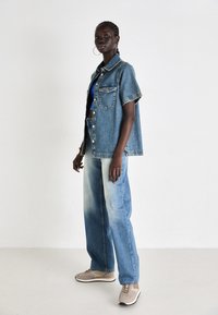 Denim skjortejakke har korte ermer, brystlomme og lyseblå farge. Kombinert med vide lyse jeans og brune sneakers.