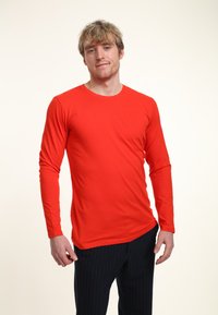 Röd långärmad skjorta i en figurnära design med rundad halsringning. Materialet verkar jämnt, med en enfärgad yta och inga synliga mönster.