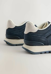 Tumedat spordijalatsid sujuva naha ja tekstureeritud seemisnahkusega. Kreemivärvi aktsendid kandadel, kontrastne hele tall ning reljeefne talla Muster.