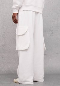 Pantalones cargo blancos hechos de una tela suave, con grandes bolsillos laterales, un ajuste relajado y un diseño sencillo sin patrones ni acentos.