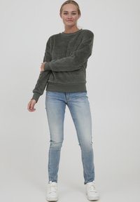 Felpa grigia in pile con polsini e orlo a costine, abbinata a jeans skinny azzurri chiari e sneakers bianche. Texture liscia, design casual.