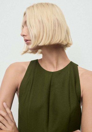 Un vestido sin mangas de color verde oscuro con un cuello alto y detalles plisados, combinado con una modelo que tiene el pelo rubio corto y lacio.