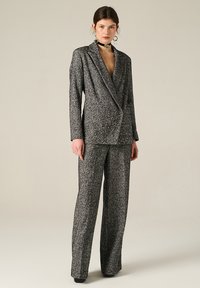 Completo in bianco e nero con texture, giacca doppiopetto e pantaloni a gamba larga, con delicati ricami metallici e una vestibilità su misura.