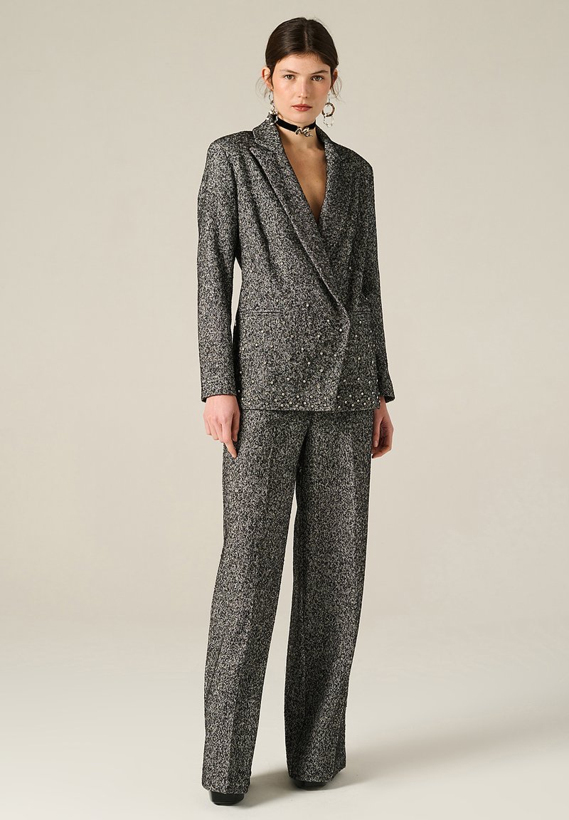 Completo in bianco e nero con texture, giacca doppiopetto e pantaloni a gamba larga, con delicati ricami metallici e una vestibilità su misura.