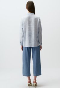 Helles blaues Langarmhemd aus Leinenstoff, mit lockerer Passform und geknöpften Manschetten, kombiniert mit weit geschnittenen hellen Denim-Hosen.