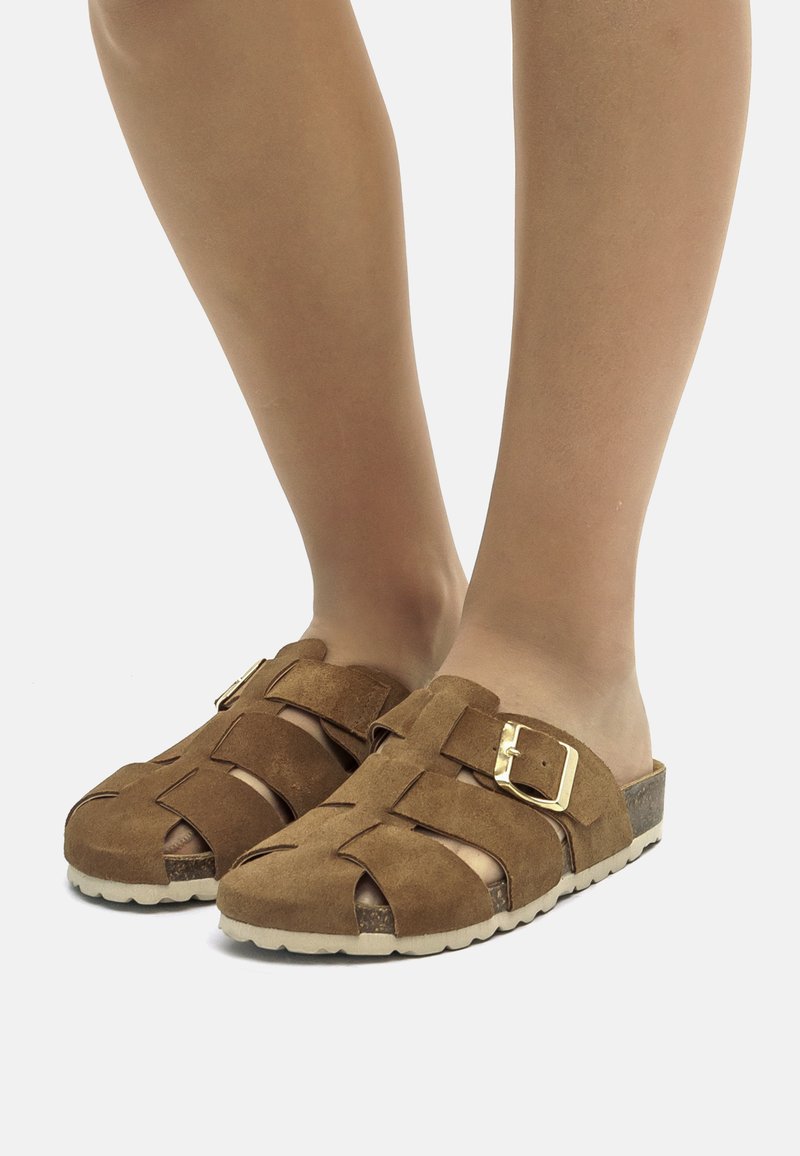 Sandales en suède marron avec un design tissé, dotées d'une boucle en or, ouvertes à l'avant et d'une semelle texturée pour une meilleure adhérence.