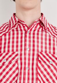 Rot-weiße karierten Hemd aus leichtem Stoff, mit einem klassischen Kragen, zwei Brusttaschen und Druckknöpfen.