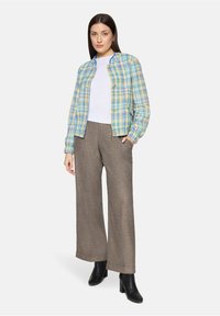 Kolorowa kurtka w kratę w odcieniach niebieskiego, zielonego i żółtego, noszona na białej bluzce; zestawiona z brązowymi szerokimi spodniami i czarnymi botkami na kostkę.