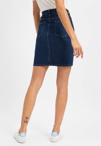 Dunkelblauer Jeans-Minirock mit taillierter Passform, Gesäßtaschen und Kontrastnähten. Kombiniert mit weißen Sneakern mit hellblauen Akzenten.