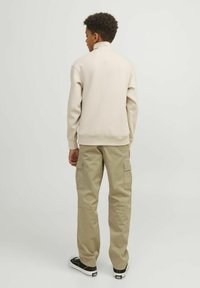 Ljust beige sweatshirt med hög krage, tillsammans med olivgröna cargobyxor. Sweatshirten har ribbad mudd och nederkant. Svarta sneakers fulländar outfiten.