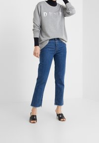Grå sweatshirt med "DKNY"-logotyp, blå högmidjade jeans och svarta öppna klackar. Jeans med rå kant. Avslappnad passform och ledig stil.