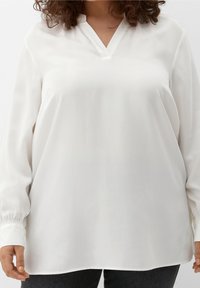 Witte blouse met lange mouwen en een V-hals. Gemaakt van gladde stof, met elastische manchetten en een relaxte pasvorm die onder de heupen valt.