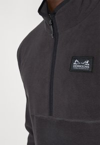 Pulover gri din fleece cu închidere cu jumătate de fermoar. Prezentă detalii cusute și un tab cu formă rectangulară neagră cu un grafic alb de munte.