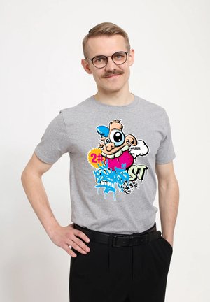 Šedé bavlněné tričko s barevnou karikovou grafikou, zahrnující postavu s velkýma očima, která nosí modrou čepici a živé akcenty.
