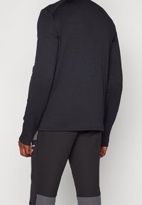 Zwarte langemouwen shirt met een textuurpatroon, voorzien van een ronde halslijn en aansluitende manchetten, gecombineerd met donkergrijze sportbroek.