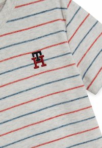 Szary bawełnowy t-shirt z czerwonymi i niebieskimi poziomymi paskami. Posiada małe wyszywane logo na lewej piersi. Wykończenie w serek.