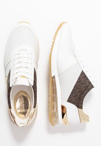 Sneaker bianche realizzate in pelle e tessuto, con design perforato, dettagli marroni e elementi in oro. Ammortizzazione ad aria trasparente nelle suole.