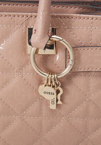 Różowa torebka o haftowanej fakturze, złotych detalach i zawieszkach w kształcie okrągłym oraz kluczy, z logo "GUESS".
