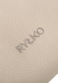 Béžová textúrovaná kožená tkanina s výrazným strieborným embosovaným logom "RYŁKO", s jemným a trvácnym povrchom.