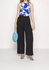 Body ajusté à motifs bleus et blancs, pantalon large noir taille haute, sac tricoté bleu clair, et sandales à talons imprimé animal.