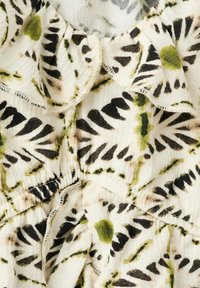 Tissu blanc avec coutures froncées et imprimé floral abstrait noir et vert en forme de rayon de soleil, montrant la texture et les bords cousus.
