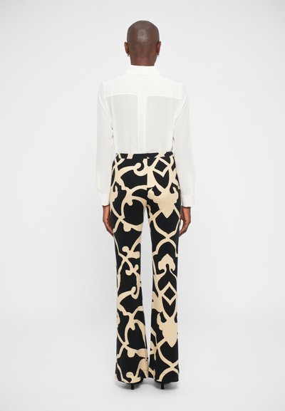 Blusa branca de manga longa com um painel transparente, combinada com calças pretas de cintura alta com padrões abstratos bege e pernas à boca de sino.